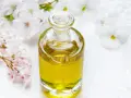 Flacone di vetro con liquido dorato, circondato da fiori bianchi e rosa. Un invito a pensare a dove buttare profumi pieni.