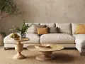 Soggiorno beige e bianco con divano modulare, tavolini in legno, piante e tappeto in juta.