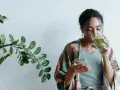 Donna con capelli ricci beve un tè verde mentre guarda il telefono, ignara che il tè fa ingrassare.