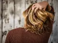 Mano tra i capelli biondi e mossi, che ricadono morbidi sulle spalle.