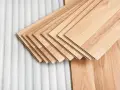 Assortimento di listoni di legno betulla colore chiaro, pronti per essere posati su un tappeto protettivo bianco.