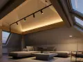 Accogliente mansarda con tetto spiovente, illuminazione soffusa e travi a vista. Un moderno sistema di faretti illumina l'ambiente, creando un'atmosfera calda e rilassante.