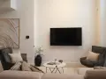 Soggiorno con TV a parete, divano, poltrone e tavolino. L'arredamento minimalista crea un'atmosfera rilassante.