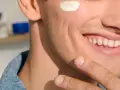 Uomo sorridente con crema sul viso, dopo la depilazione con rasoio. Pelle liscia e curata.