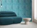Divano blu petrolio davanti a una parete con motivo floreale su sfondo colore verde acqua. Tavolino beige e lampada nera.