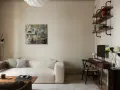 Soggiorno accogliente con divano bouclé bianco, quadro astratto e scrivania. Le **pareti colore crema** creano un'atmosfera calda e rilassante.