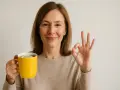 Woman holding a yellow mug with lemon and giving an OK sign.