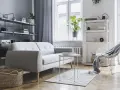 Soggiorno moderno con divano grigio, tavolino bianco, cestini in paglia e scaffali pieni di oggetti. Ottime idee arredamento casa per uno stile minimalista.