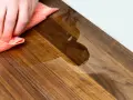 Mano che pulisce un tagliere di legno con un panno umido. Scopri come pulire il tagliere di legno per mantenerlo igienico e bello.