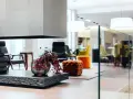 Interni open space di case moderne: camino con legna, vasi con bacche rosse, sedie colorate e pouf arancioni in un ambiente luminoso.
