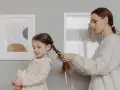 Mamma intreccia i capelli della bambina, creando bellissime acconciature. La piccola tiene un pupazzo a forma di gatto.