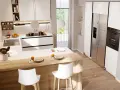 Modern white kitchen with a wooden island, bar stools, stainless steel fridge, and oven.