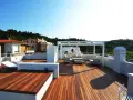 Terrazza sul tetto idee: un salotto all'aperto con divani, poltrone e tavolino sotto un pergolato bianco. Sdraio e vista su case e colline verdi.