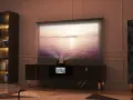 Mobile nascondi TV con proiettore integrato, schermo su cui scorre un tramonto sul mare, libreria e mobile decorato.
