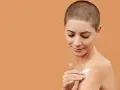 Donna con capelli corti applica crema idratante al burro di karitè viso sulla spalla, per una pelle morbida e nutrita.