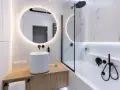 Moderno bagno con lavabo bianco su mobile in legno, specchio rotondo illuminato e vasca da bagno. Ottime bagno cieco idee.