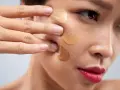 Dita che sfumano campioni di fondotinta sulla guancia per capire come scegliere il colore del fondotinta perfetto.