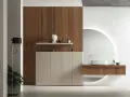 Bagno elegante e raffinato con mobile in legno, lavabo sospeso, specchio circolare retroilluminato e un tocco di verde da una pianta.