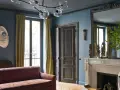 Soggiorno elegante con divano bordeaux, pareti blu balena e tendaggi dorati. Un camino in marmo e sculture africane completano l'arredo.