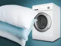 Impara come lavare i cuscini in lavatrice per un sonno fresco e igienico. Cuscini bianchi e azzurri accanto a una lavatrice bianca.