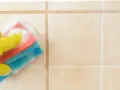 Mano con guanto giallo pulisce piastrelle del bagno con spugna schiumosa.