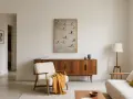 Un soggiorno in stile wabi sabi con poltrona in lana bouclé, credenza in legno e quadro di oche in volo.
