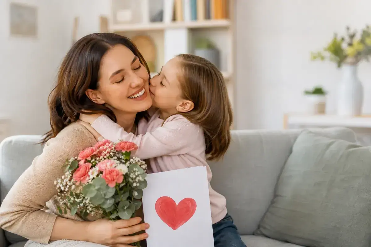 Bambina bacia la mamma, regalandole fiori e un disegno a forma di cuore. Un dolce momento per la festa della mamma.