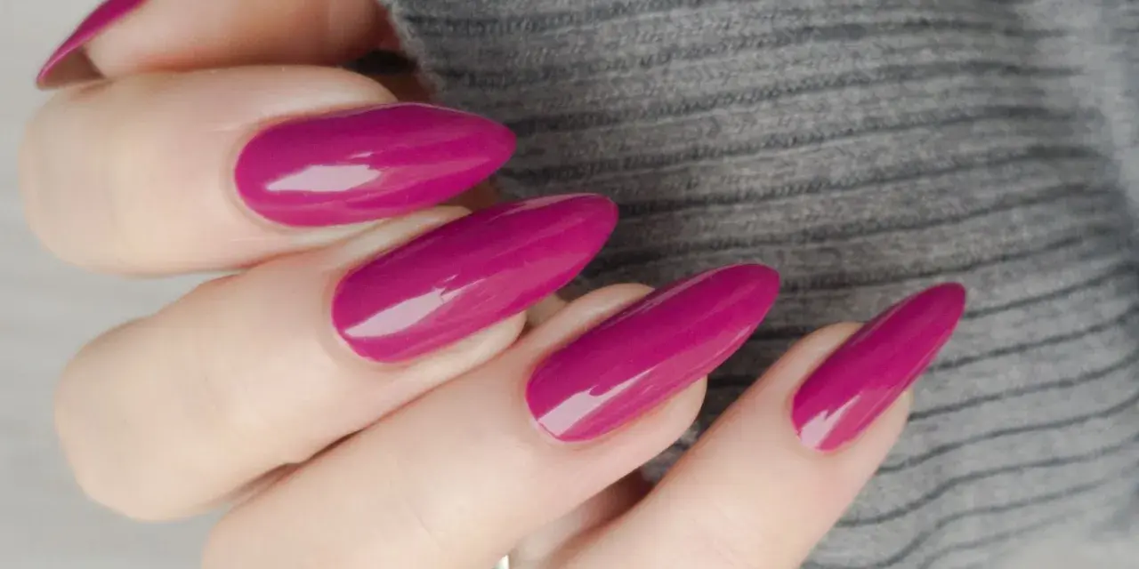 Mano con unghie lunghe e affusolate, smalto color ciliegia brillante, su sfondo grigio melange.