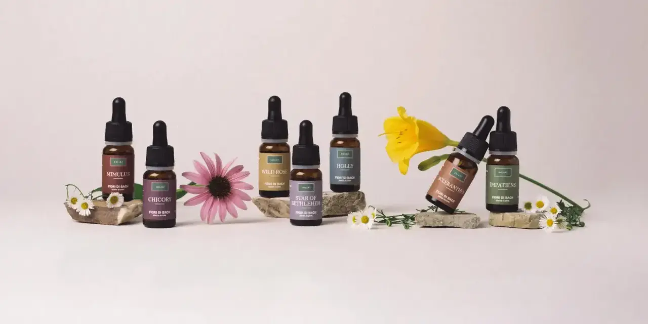 Flaconi di Fiori di Bach Rescue Remedy con Mimulus, Chicory, Wild Rose, Star of Bethlehem, Holly, Scleranthus e Impatiens, circondati da fiori.