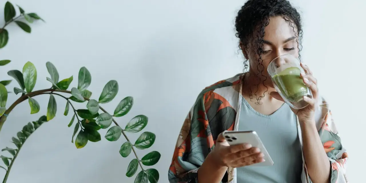 Donna con capelli ricci beve un tè verde mentre guarda il telefono, ignara che il tè fa ingrassare.