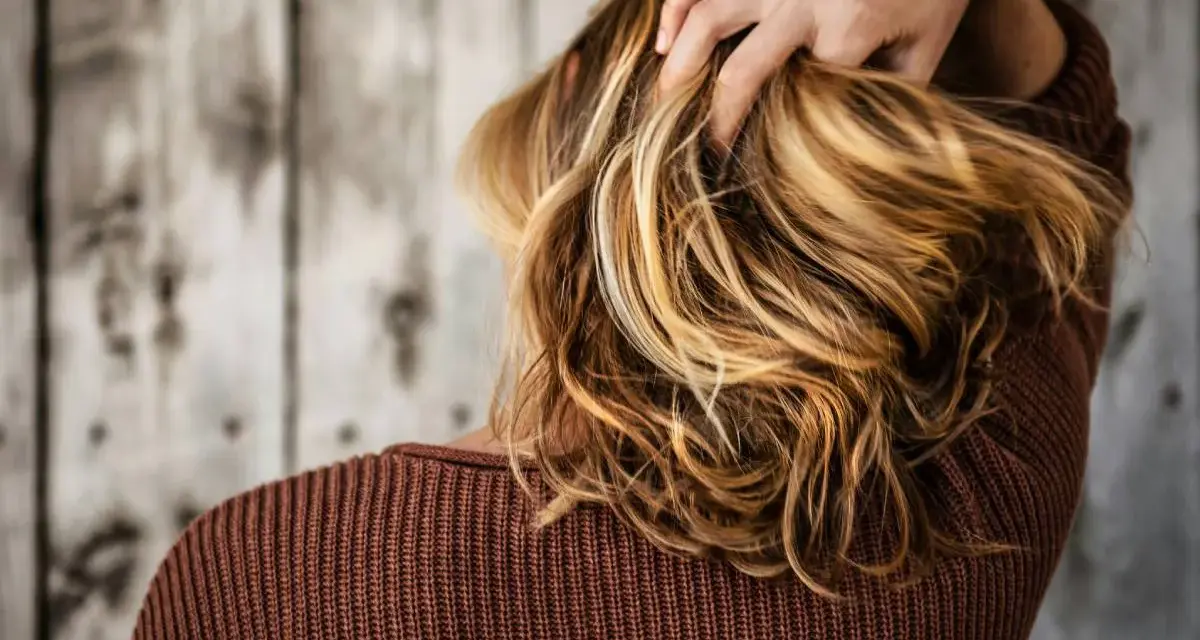 Mano tra i capelli biondi e mossi, che ricadono morbidi sulle spalle.