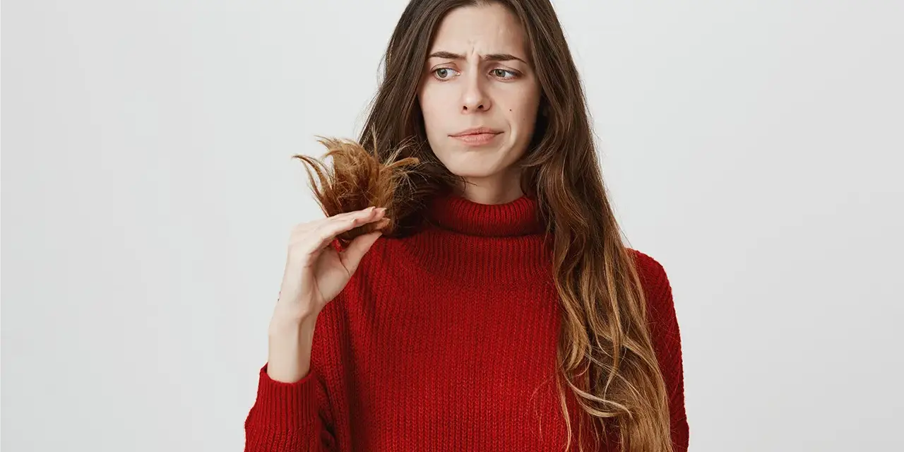 Donna preoccupata guarda le doppie punte, pensando a come nutrire i capelli per renderli sani e forti.
