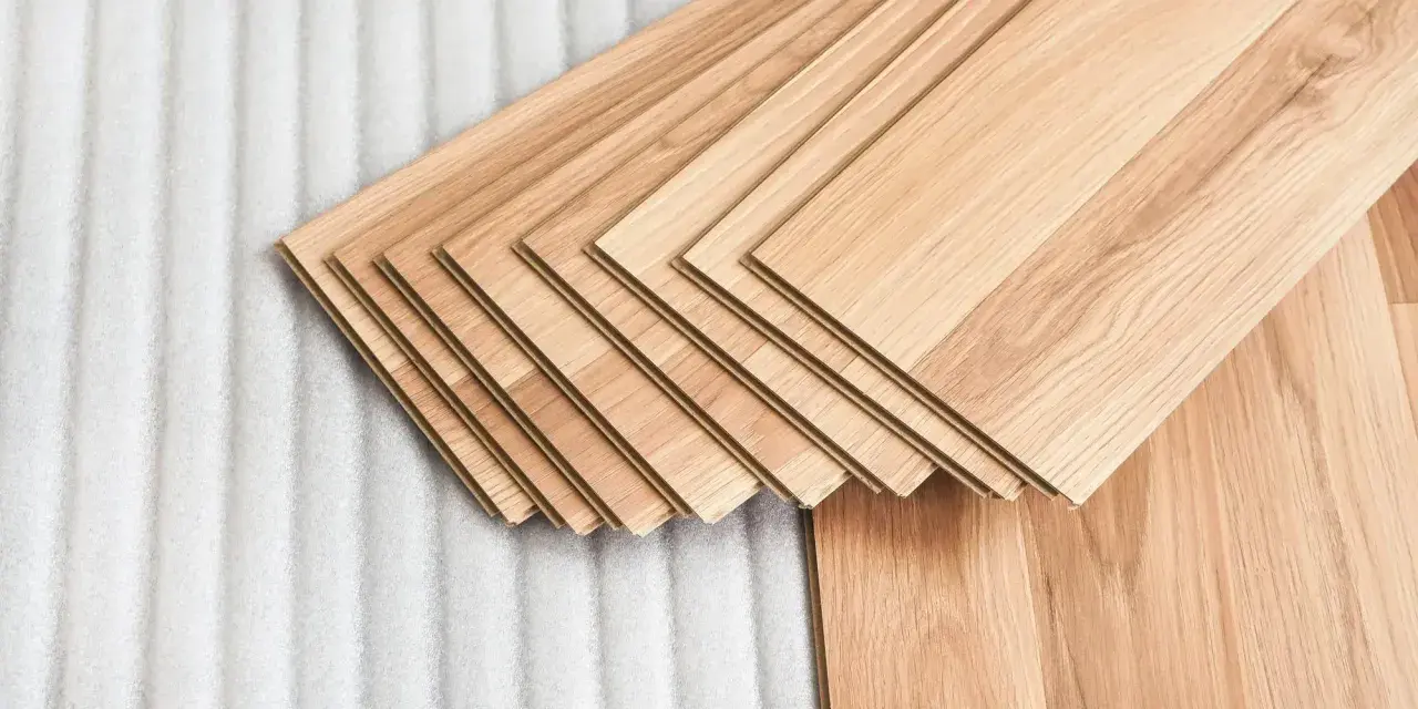 Assortimento di listoni di legno betulla colore chiaro, pronti per essere posati su un tappeto protettivo bianco.