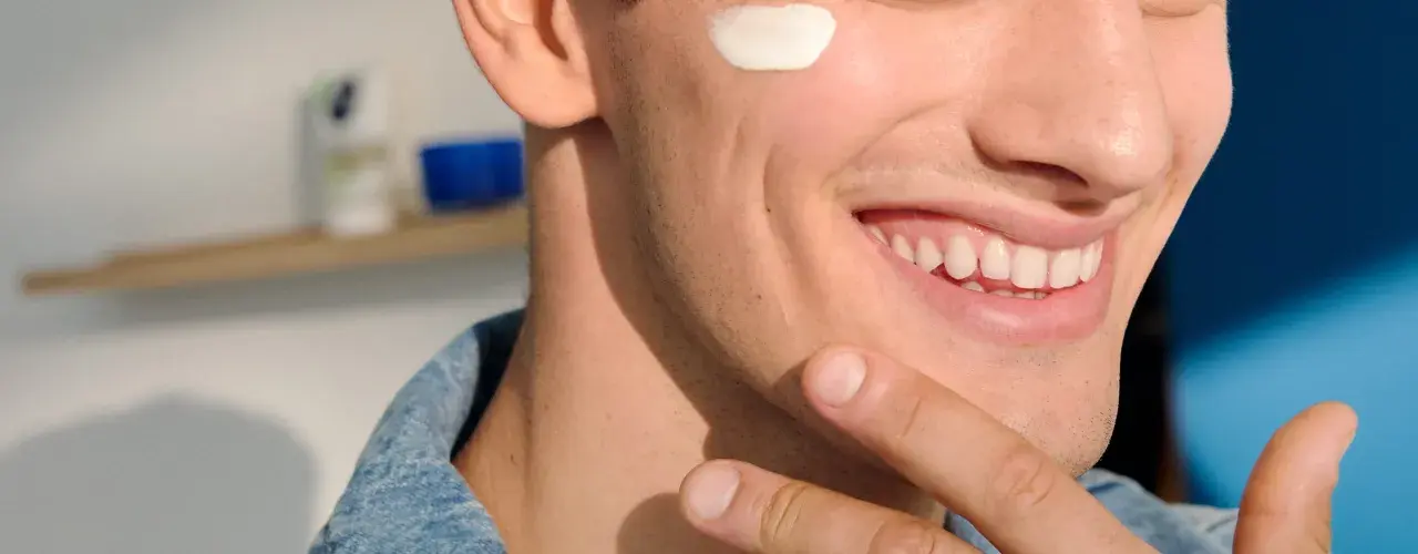 Uomo sorridente con crema sul viso, dopo la depilazione con rasoio. Pelle liscia e curata.