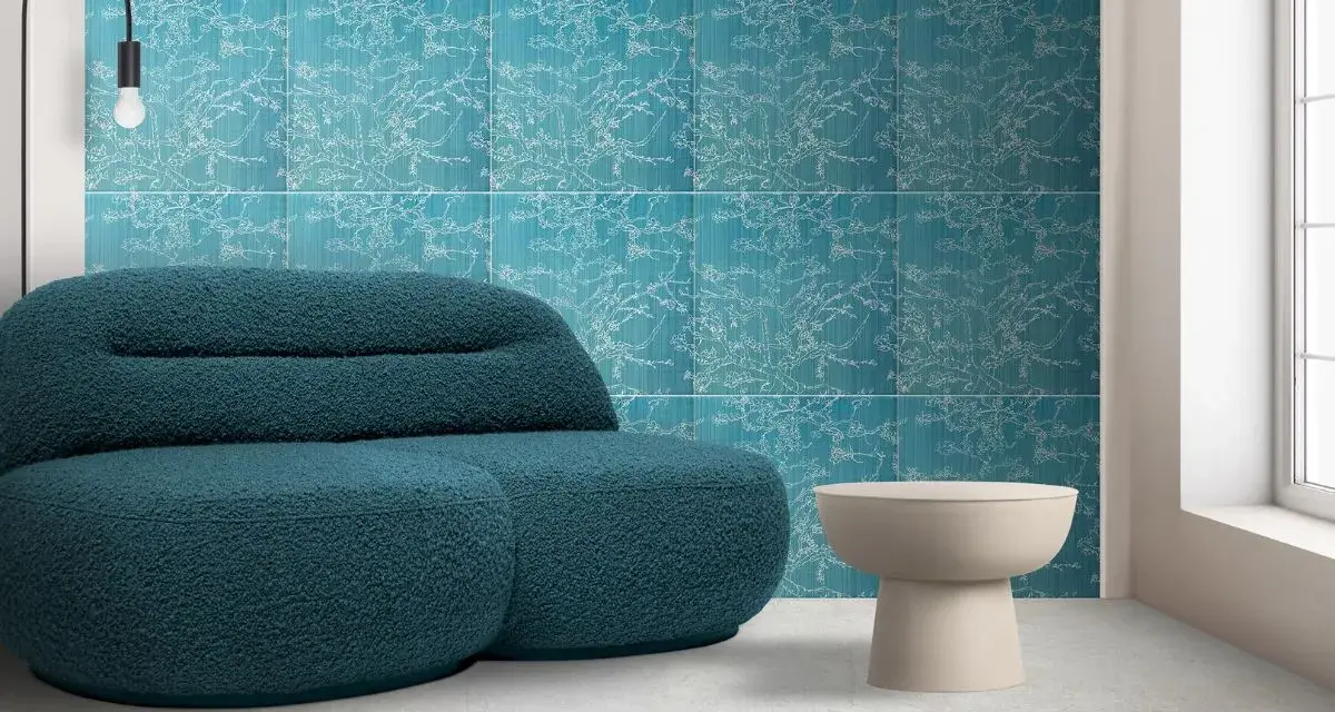 Divano blu petrolio davanti a una parete con motivo floreale su sfondo colore verde acqua. Tavolino beige e lampada nera.