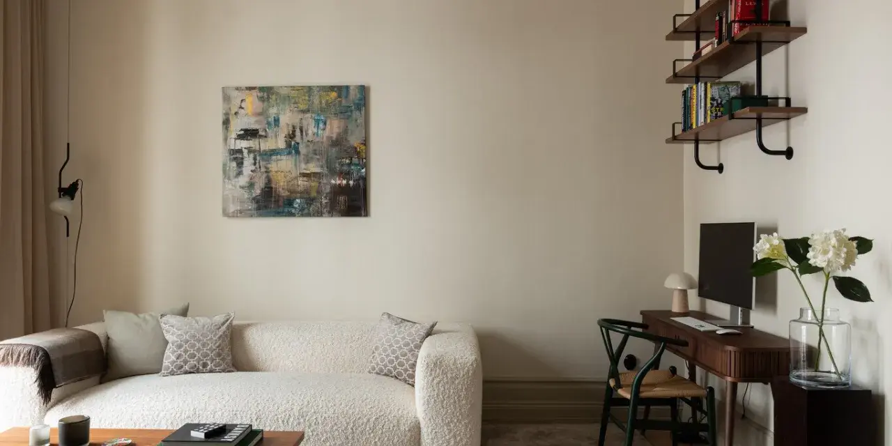 Soggiorno accogliente con divano bouclé bianco, quadro astratto e scrivania. Le **pareti colore crema** creano un'atmosfera calda e rilassante.
