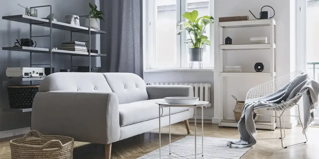 Soggiorno moderno con divano grigio, tavolino bianco, cestini in paglia e scaffali pieni di oggetti. Ottime idee arredamento casa per uno stile minimalista.