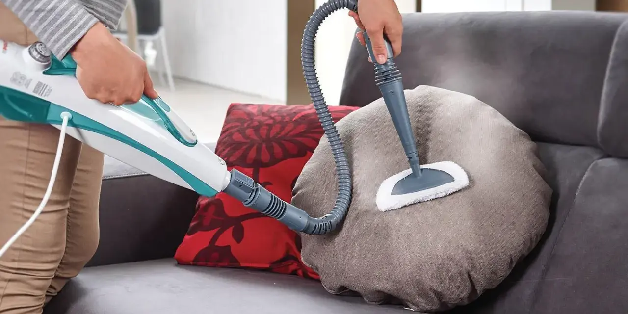 Persona usa un pulitore a vapore per pulire un cuscino del divano in tessuto. Scopri come pulire divano in tessuto con questo metodo efficace.