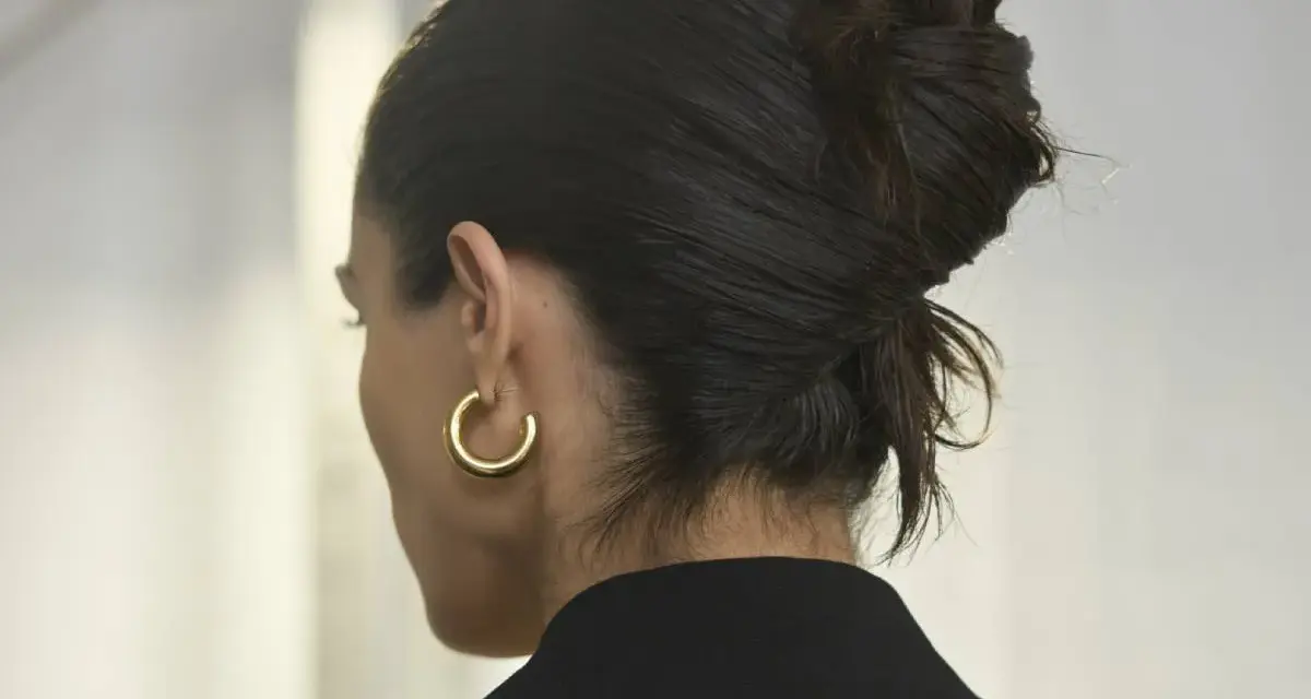 Capelli scuri raccolti in un chignon semplice, con un orecchino a cerchio dorato.