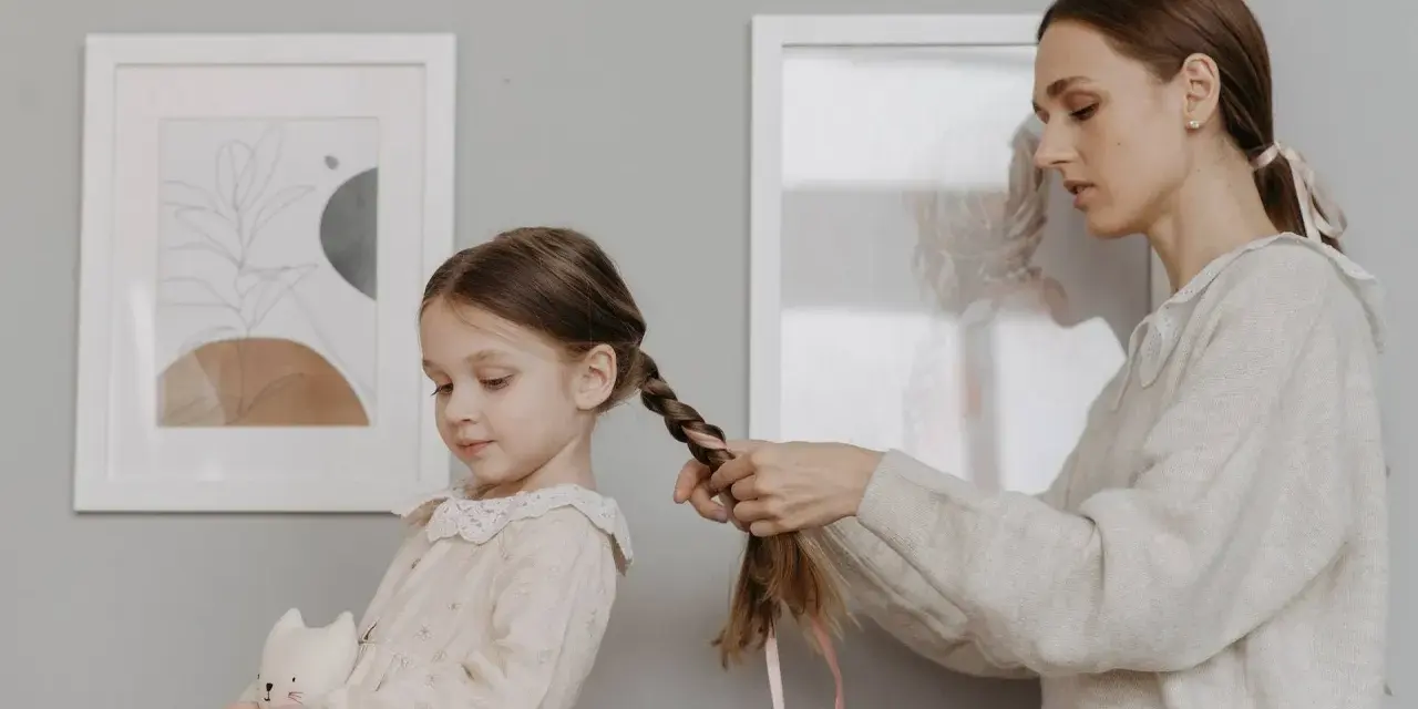 Mamma intreccia i capelli della bambina, creando bellissime acconciature. La piccola tiene un pupazzo a forma di gatto.