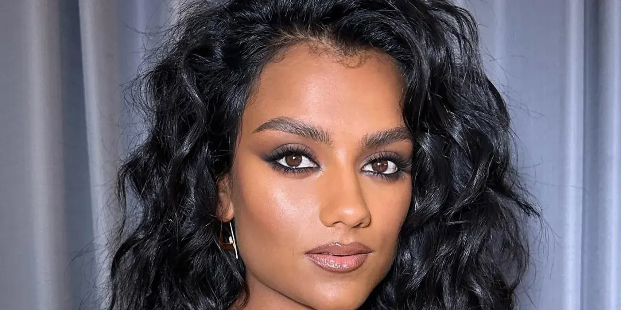 Capelli neri e ondulati, lucidi grazie al hair oiling, incorniciano il viso di una donna con trucco intenso.