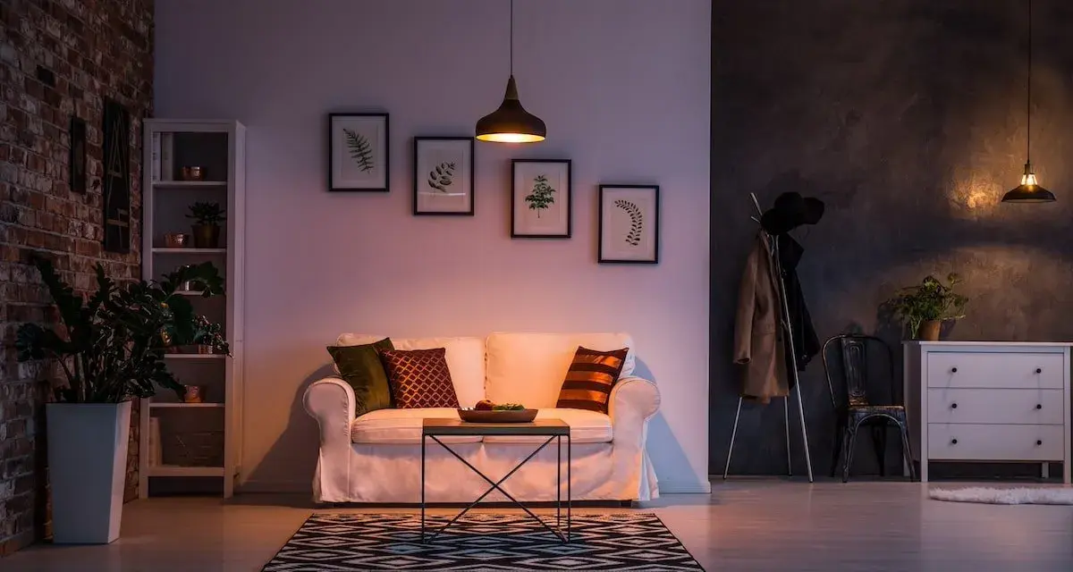 Un divano bianco accogliente, con cuscini colorati, in un soggiorno con mattoni a vista e quadri botanici. Atmosfera di puro stile cozy.