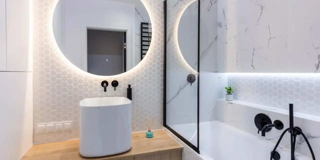 Moderno bagno con lavabo bianco su mobile in legno, specchio rotondo illuminato e vasca da bagno. Ottime bagno cieco idee.