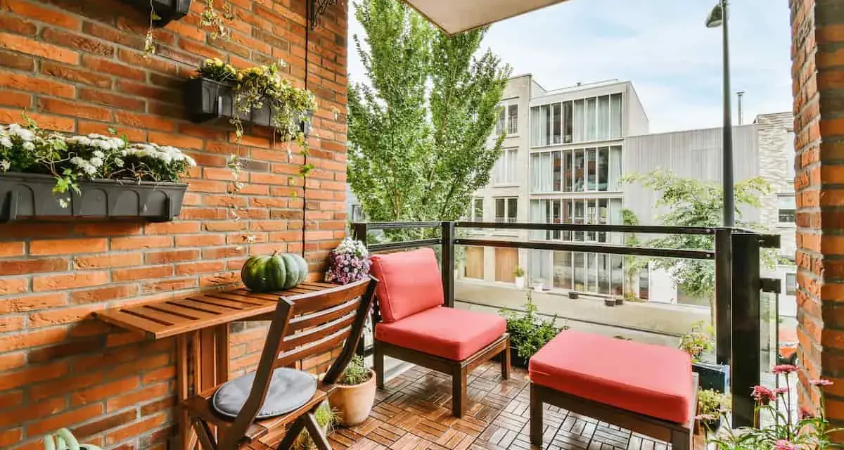 Arredare terrazzo appartamento: un angolo relax con sedie rosse, tavolino in legno e piante su muro di mattoni.