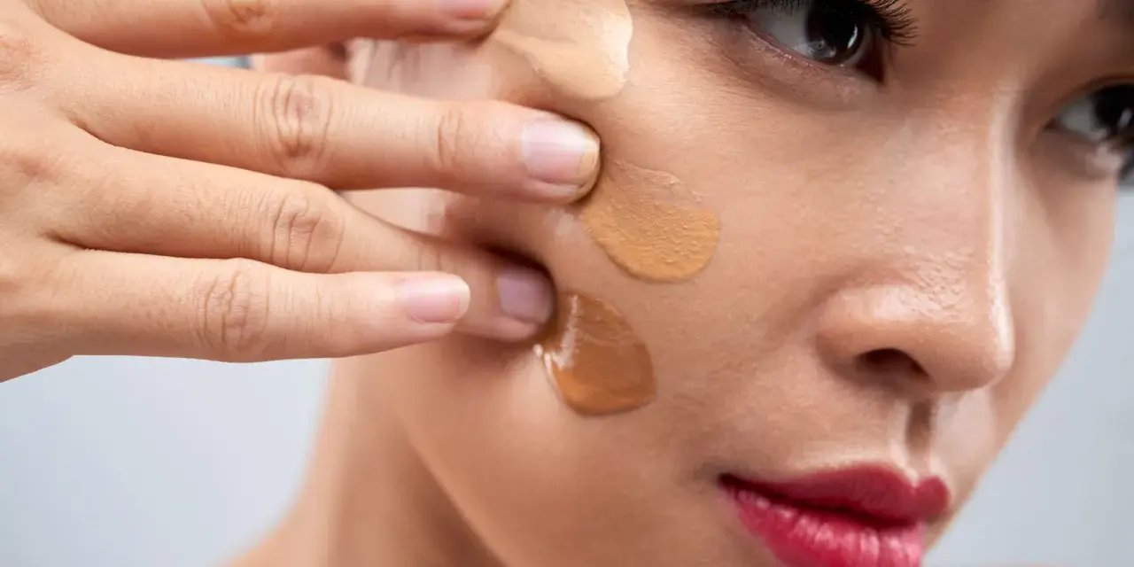 Dita che sfumano campioni di fondotinta sulla guancia per capire come scegliere il colore del fondotinta perfetto.