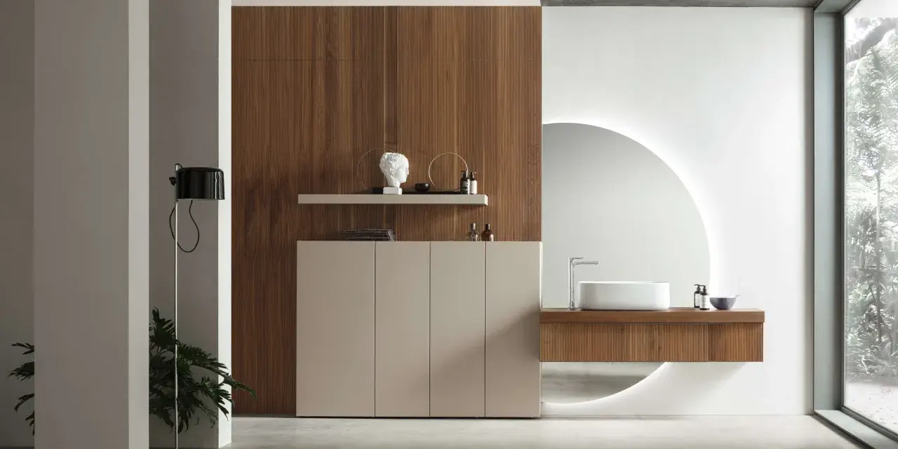 Bagno elegante e raffinato con mobile in legno, lavabo sospeso, specchio circolare retroilluminato e un tocco di verde da una pianta.