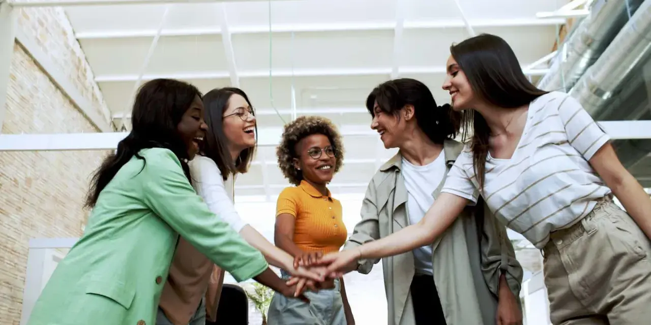Cinque donne sorridono, unendo le mani in un gesto di unione e **empowerment femminile**.