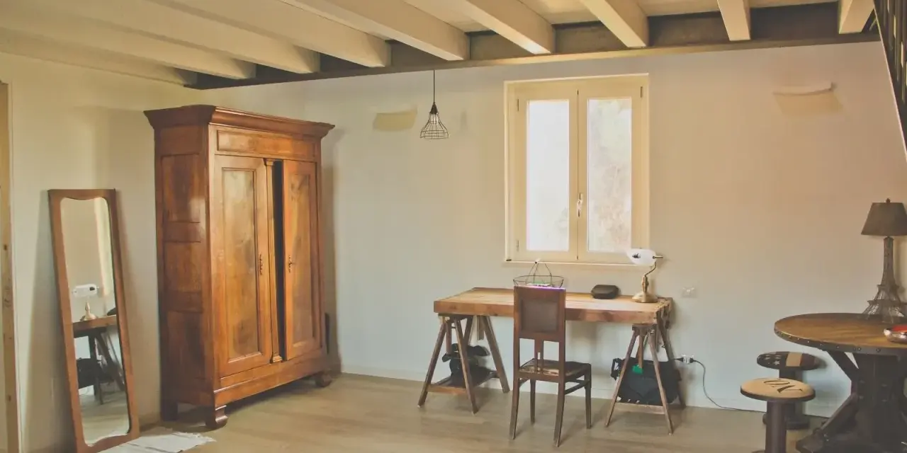 Interni di case di campagna: armadio antico, scrivania rustica e specchio a figura intera creano un'atmosfera accogliente.