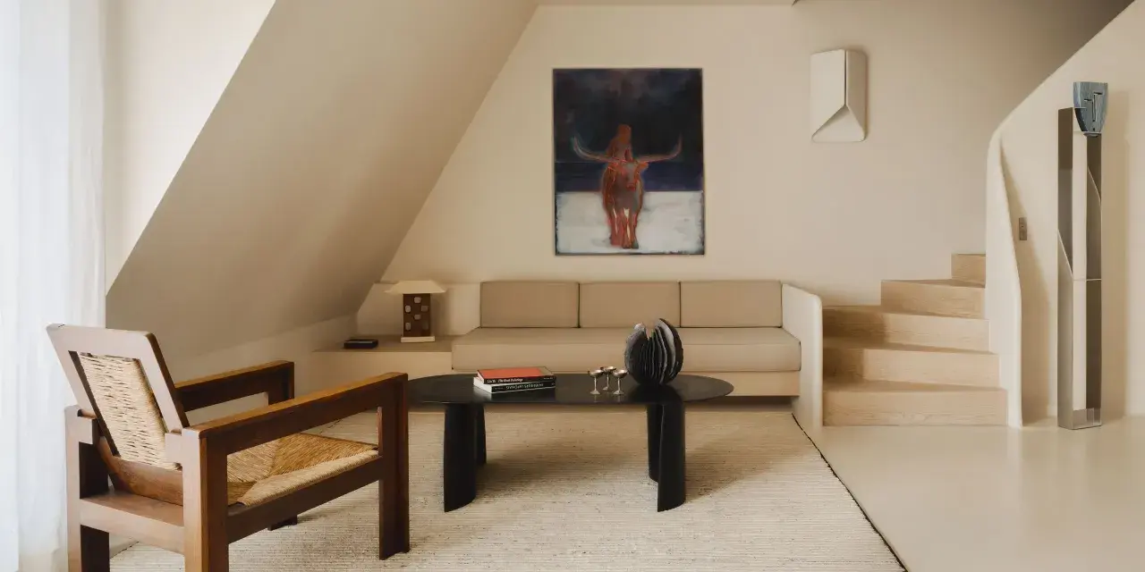 Arredamento minimal soggiorno: poltrona in legno e paglia, divano beige, tavolino nero con libri e scultura, quadro astratto con toro.