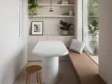 Un angolo accogliente con tavolo bianco, sgabello in legno e piante. Un'ispirazione su come combattere la solitudine in casa, creando spazi piacevoli.